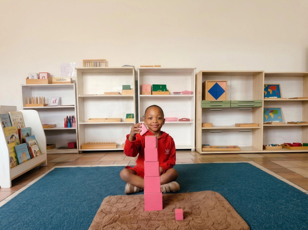A young Addnum ECD learner smiling while building a pink block tower on a classroom mat